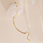 The Herringbone Bracelet features a sleek gold chain design, elegantly displayed over a white crystal on a light beige background.