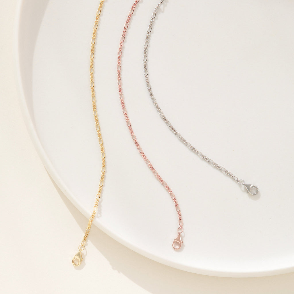 Three delicate unisex Figaro Bracelets in gold, rose gold, and silver—each reflecting modern jewelry style—are elegantly displayed on a white plate.