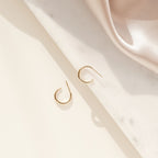 Chloe Hoops gold hoop earrings rest on a cream and marble surface with soft beige satin, offering polished bands that make the perfect everyday accessory for timeless elegance.