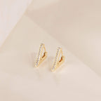Ezra Triangle Earrings: gold geometric earrings with a vertical bar design and a pave of sparkling crystals, displayed on a beige surface.