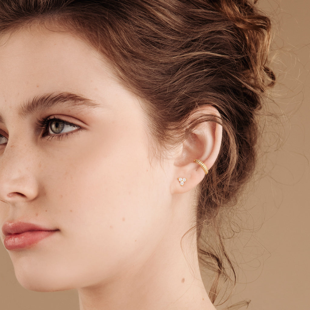 Close-up of a young woman with brown hair, wearing a gold ear cuff and an earring stack featuring delicate Lily Studs.