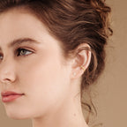 Close-up of a young woman with brown hair, wearing a gold ear cuff and an earring stack featuring delicate Lily Studs.