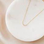 Dainty gold necklace featuring a moon pendant set with small sparkling stones, displayed on a round white marble dish against a soft blush satin background. 