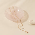 A gold Figaro chain necklace elegantly draped over a polished, rose quartz bowl. The alternating pattern of short and elongated oval links is distinct, adding visual texture and a classic Italian-inspired design to the fine gold piece.