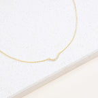 The Lucia Pave Necklace is a delicate gold chain with a small crescent charm pendant adorned with tiny crystals, beautifully displayed on a white surface.