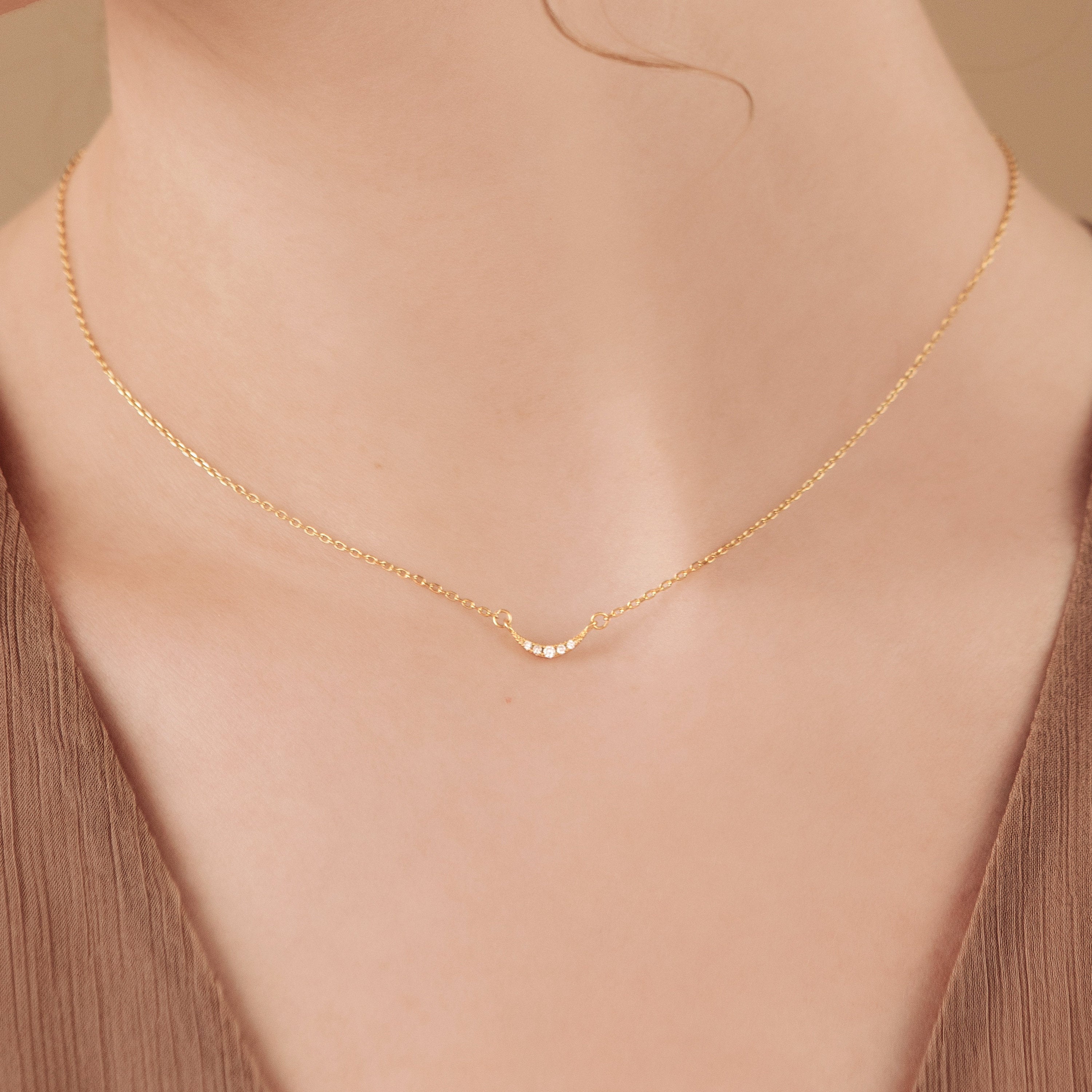 Close-up of a woman's neck wearing the Lucia Pave Necklace, a delicate gold piece featuring a small crescent charm pendant.