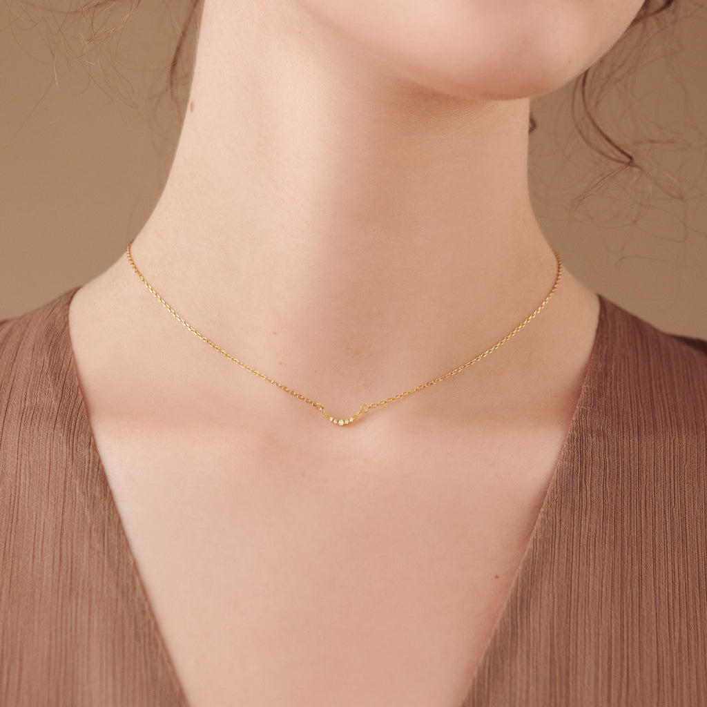 Close-up of a woman's neck wearing the Lucia Pave Necklace, featuring a delicate gold chain with a small crescent charm.