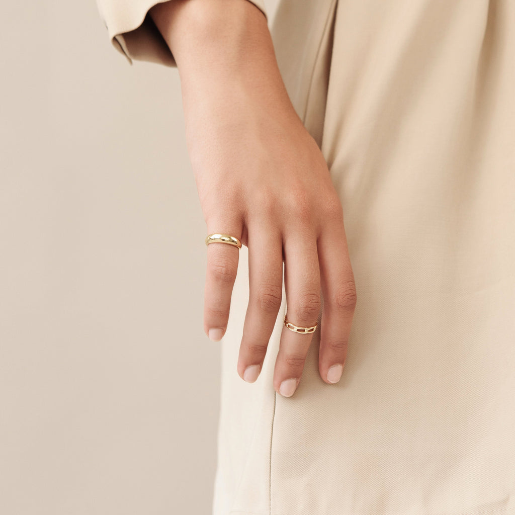 A woman wearing the gold Dome Ring on her middle finger, paired with a thin gold band, with her hand resting by her side in a neutral-toned outfit.