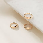 The Twisted Dome Ring, a textured gold accessory, is showcased alongside two twisted gold rings on a light marble surface with a cream background.