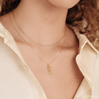 Close-up of a woman in a cream shirt wearing two gold necklaces, showcasing elegant layering with a Dainty Link Chain Necklace in Rose Gold and an Arabic name pendant.