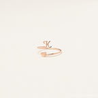 The Initial Heart Wrap Ring features a gold band with a letter K and a heart on opposite ends—an elegant symbol of love. Personalize it with any initial for a unique touch, beautifully displayed against a plain backdrop.