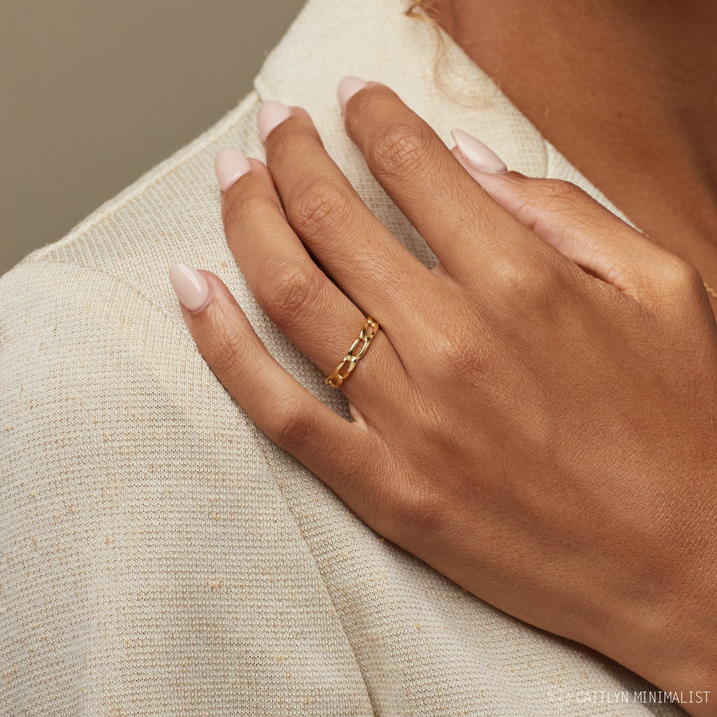 Close-up of a woman’s hand resting on her shoulder, wearing the delicate 3 mm link ring in 18K gold.