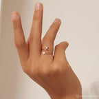 A hand wears two delicate rings, including the Initial Heart Wrap Ring—one with a heart and one with the letter K—set against a neutral background, perfect for customizing with initials as a symbol of love.