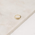 The Pave Signet Ring, adorned with a cluster of small diamonds, rests on a light marble surface, offering a modern-luxe statement accessory.