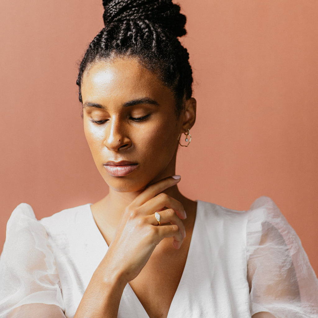 A woman with her hand on her chin highlights a modern-luxe look, featuring the Pave Signet Ring as her statement accessory.