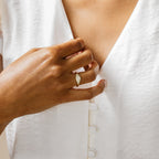 Wearing the Pave Signet Ring as a bold statement piece, a person touches their chest while dressed in a white button-up shirt, showcasing modern-luxe style.
