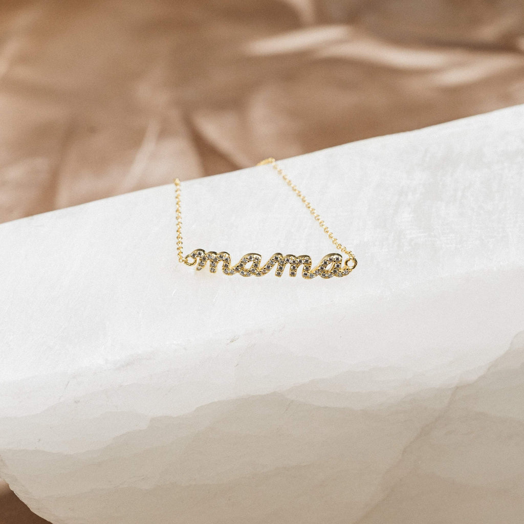 A sparkling Pave Mama Script Bracelet, featuring "mama" in elegant script and shown on a white textured surface—a timeless jewelry piece perfect for celebrating motherhood.
