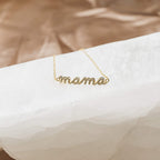 A sparkling Pave Mama Script Bracelet, featuring "mama" in elegant script and shown on a white textured surface—a timeless jewelry piece perfect for celebrating motherhood.