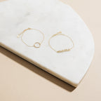 Two delicate gold bracelets rest on a white marble slab; one features a ring, while the other is the Pave Mama Script Bracelet—perfect for celebrating mama jewelry and the beauty of motherhood.