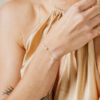 A woman wears the Mini Lily Diamond Bracelet, featuring small flower charms, paired with a satin gold halter top.