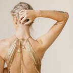 A woman in a gold halter dress, back to the camera and hand in her hair, displays her tattoos and the Mini Lily Diamond Bracelet, adding sparkle to her jewelry collection.