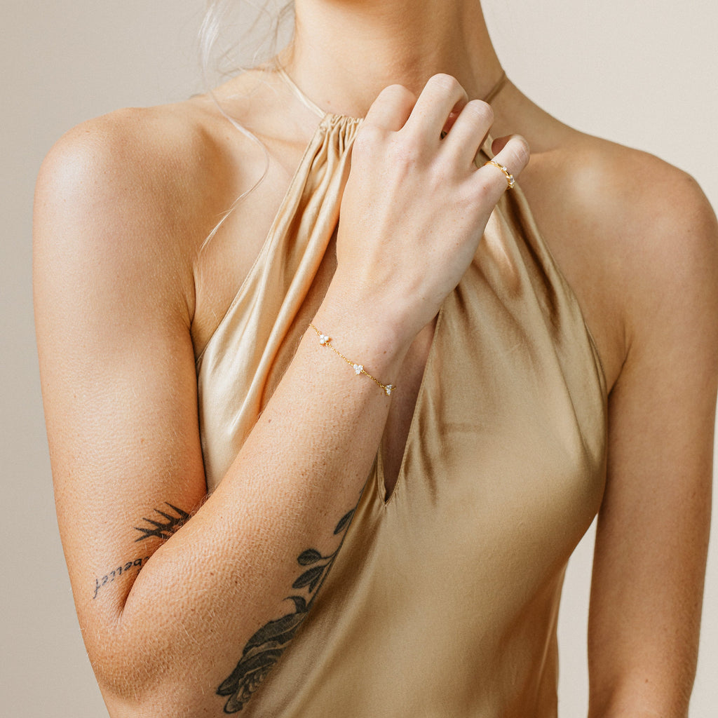 A woman in a gold halter dress with a floral tattoo on her arm showcases the Mini Lily Diamond Bracelet.