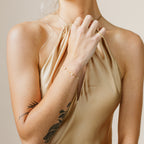 A woman in a gold halter dress with a floral tattoo on her arm showcases the Mini Lily Diamond Bracelet.
