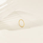 The Lea Twisted Ring, featuring polished bands, rests on a light surface next to a clear, textured glass object.