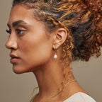 Profile of a woman with curly hair, wearing the Margot Pearl Hoops and a matching gold necklace.