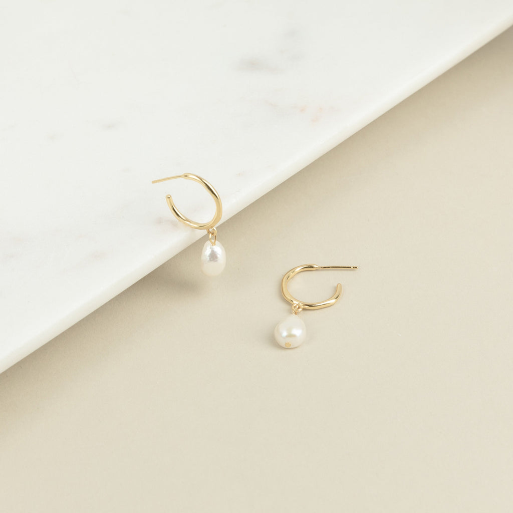 The Margot Pearl Hoops are gold earrings featuring an elegant drop pearl.