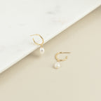 The Margot Pearl Hoops are gold earrings featuring an elegant drop pearl.