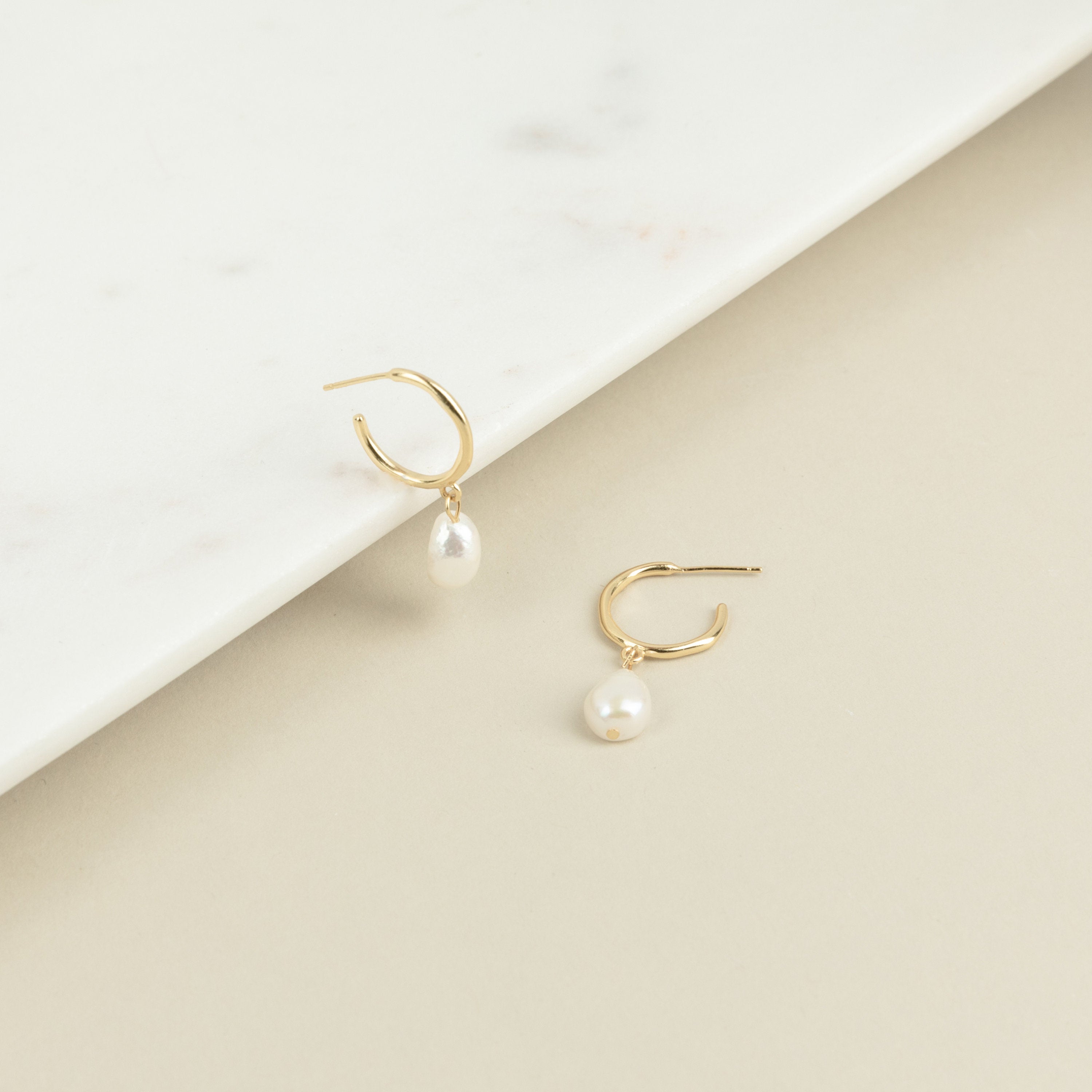 The Margot Pearl Hoops are gold earrings featuring an elegant drop pearl.