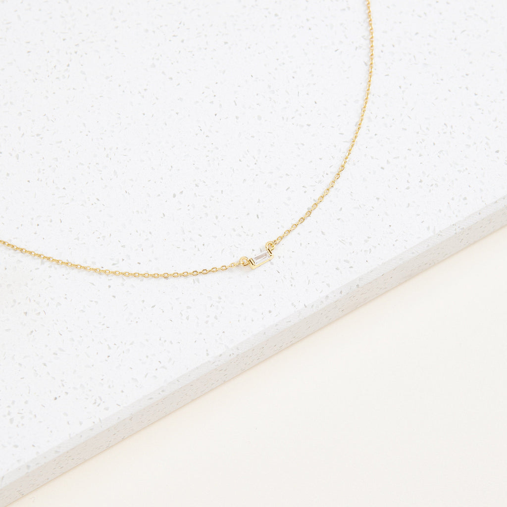 The Emery Necklace in Sterling Silver features a rectangular pendant, making it an ideal minimal necklace for a thoughtful holiday gift. Displayed elegantly on a white speckled surface.