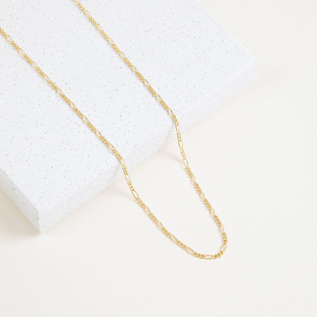 Close-up of the Figaro necklace laid over a white speckled tile surface, highlighting the alternating link pattern.