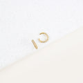 The Mia Pave Cuffs, gold hoop earrings adorned with small clear stones, sparkle beautifully on a white speckled surface.