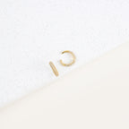 The Mia Pave Cuffs, gold hoop earrings adorned with small clear stones, sparkle beautifully on a white speckled surface.