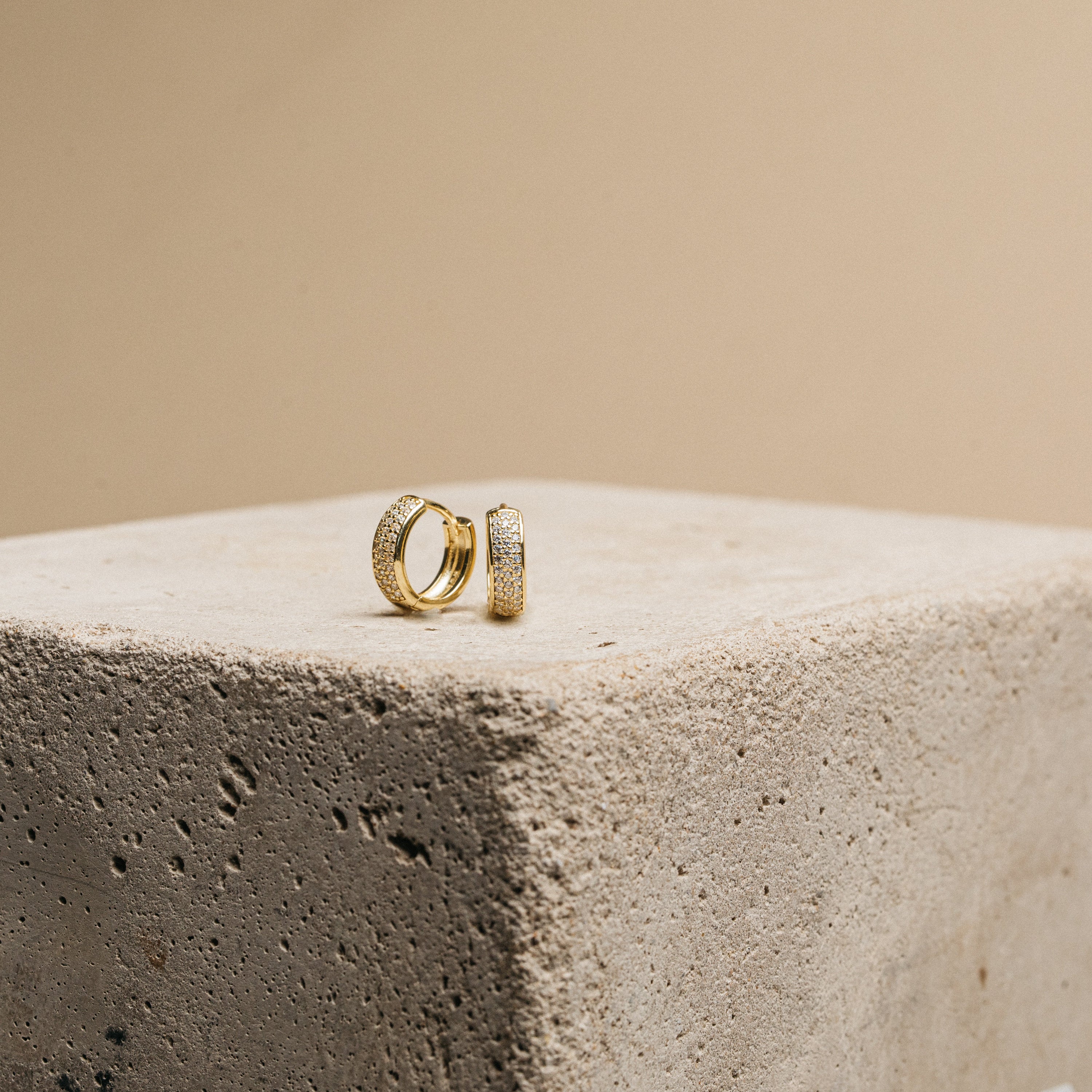 Pave Diamond Huggies, featuring small diamonds, displayed on a textured concrete block with a beige background—an elegant essential for your jewelry box.