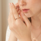 A woman wears a delicate gold Twisted Birthstone Ring featuring a small black stone on her finger as she gently touches her face.