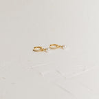 Mae Huggies: Gold hoop earrings accented with pearls and small crystals are displayed on a textured white surface—perfect for those who love timeless pearl huggies.