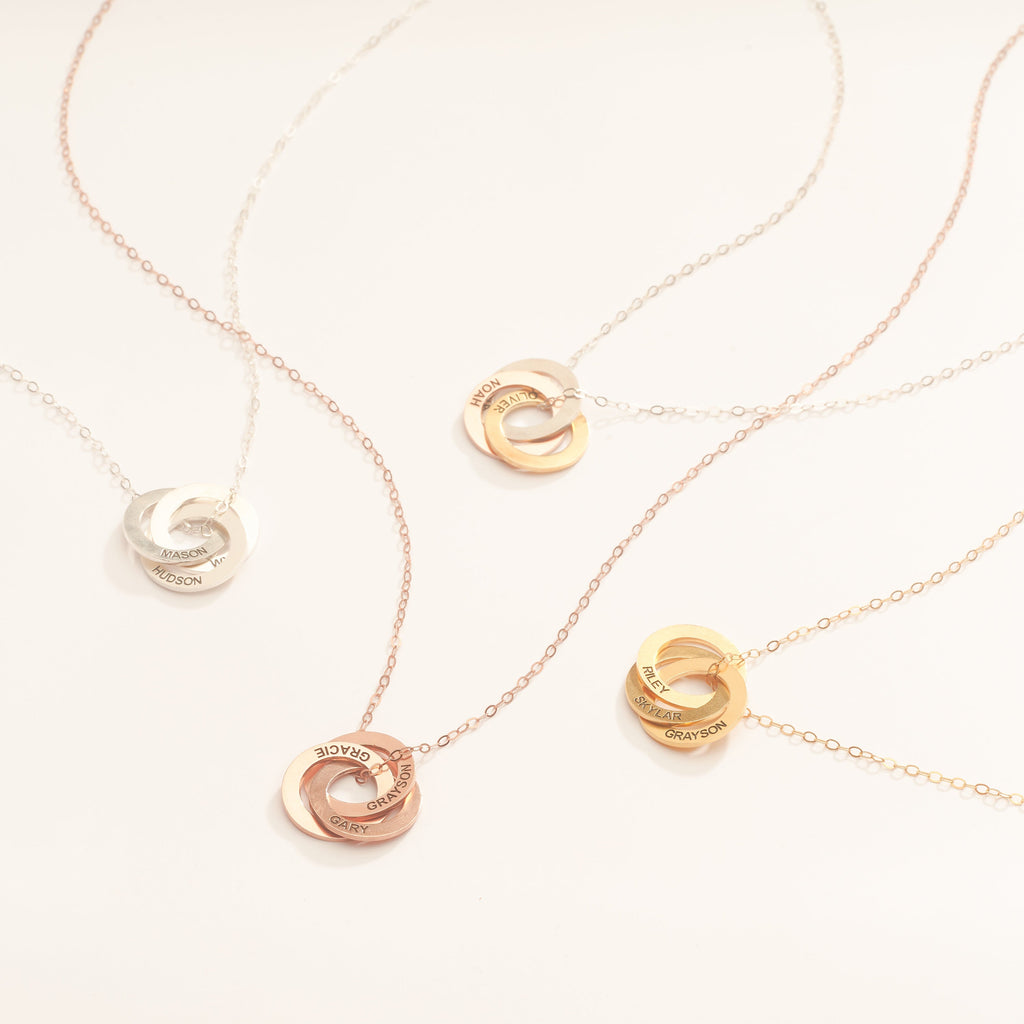 The Interlocking Family Necklace features four intertwined circles in silver, rose gold, and gold on a light background—ideal as a custom engraved gift for loved ones.
