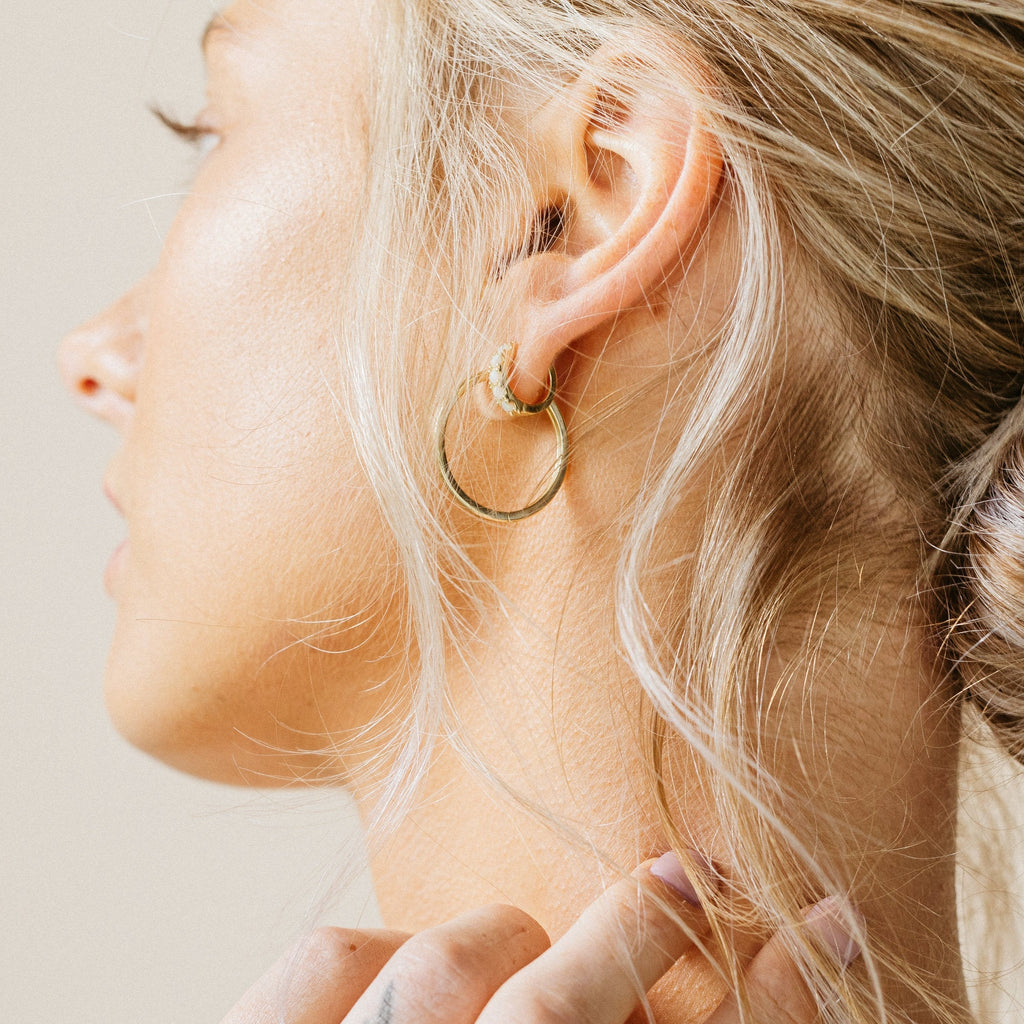 Close-up of a woman with blonde hair wearing Opal Huggies earrings, touching her neck.