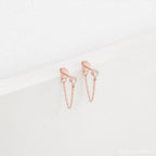 Birthstone Chain Studs in rose gold feature clear gemstones and a delicate chain, shown on a white textured background—versatile earrings ideal for any occasion.