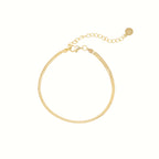 The Herringbone Anklet features a delicate gold chain with an adjustable clasp and small round charm, perfect for a minimalist jewelry style or polished ankle look. Displayed on a white background.