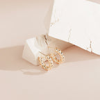 Remi Twist Hoops showcased on white textured blocks atop a soft beige surface—perfect for minimal jewelry lovers.