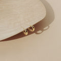 Dome Hoops in gold are displayed on the edge of a light wooden tray set against a beige background.