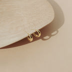 Dome Hoops in gold are displayed on the edge of a light wooden tray set against a beige background.