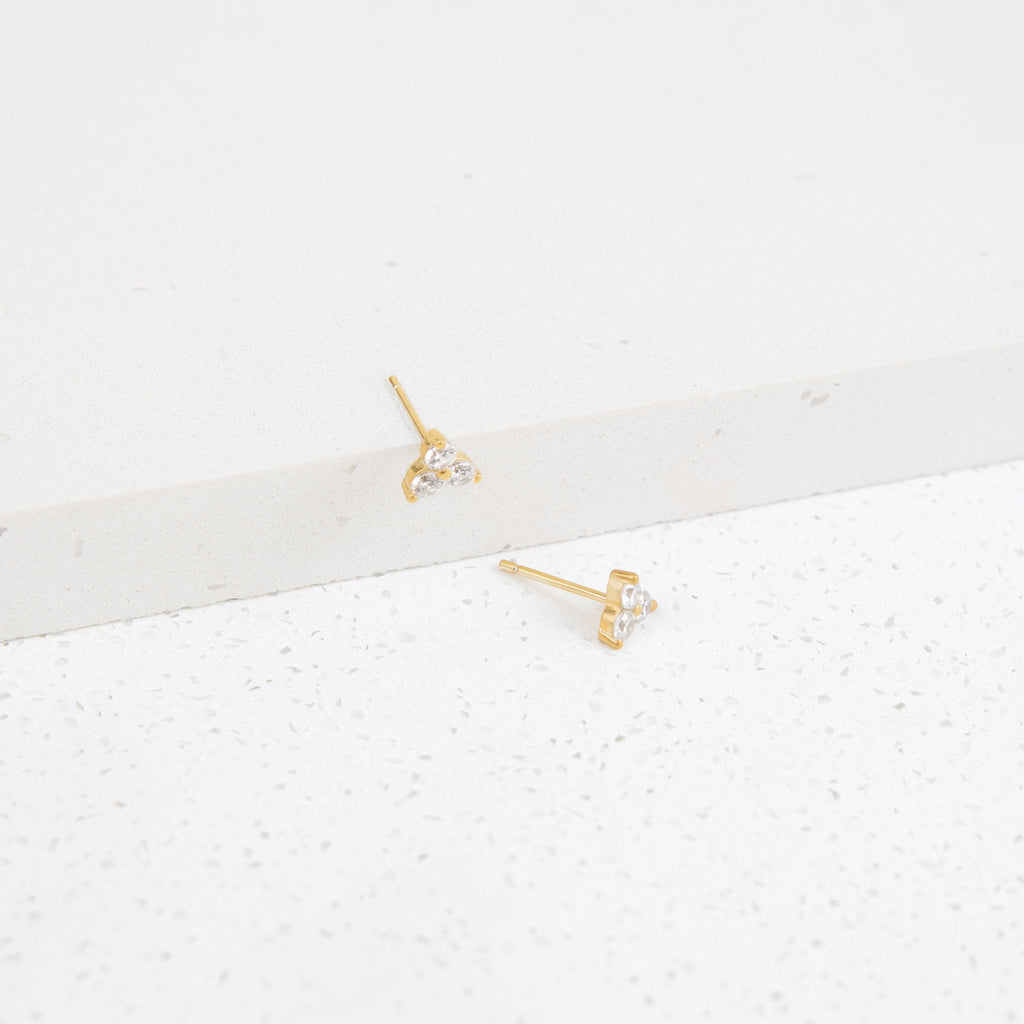 Lily Studs: Gold earrings featuring three small clear stones each, perfect for stacking. Displayed on a white textured surface.