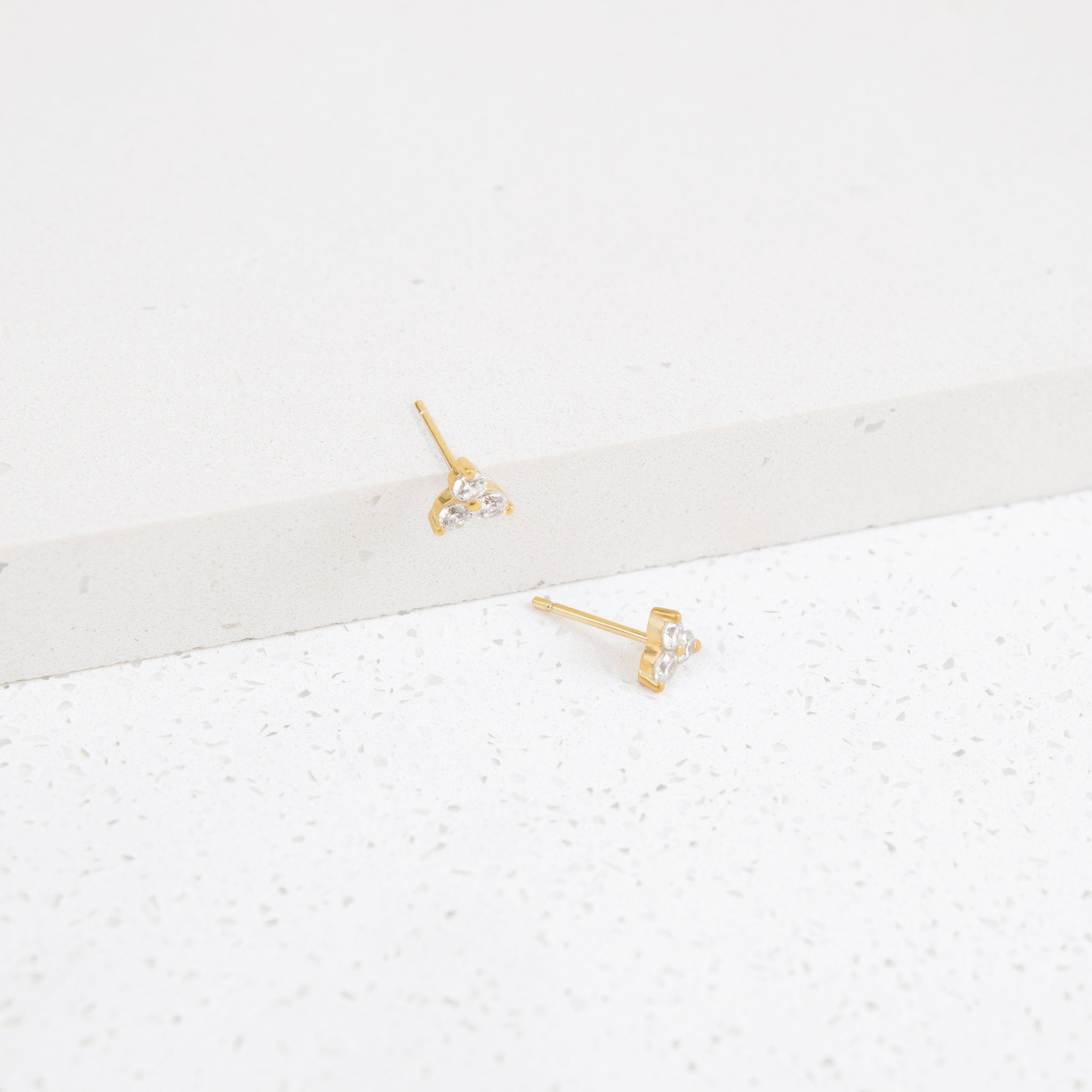 Lily Studs: Gold earrings featuring three small clear stones each, perfect for stacking. Displayed on a white textured surface.