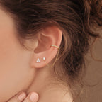 Close-up of an ear adorned with a stylish earring stack, featuring Lily Studs and a gold ear cuff connected by a delicate gold chain.