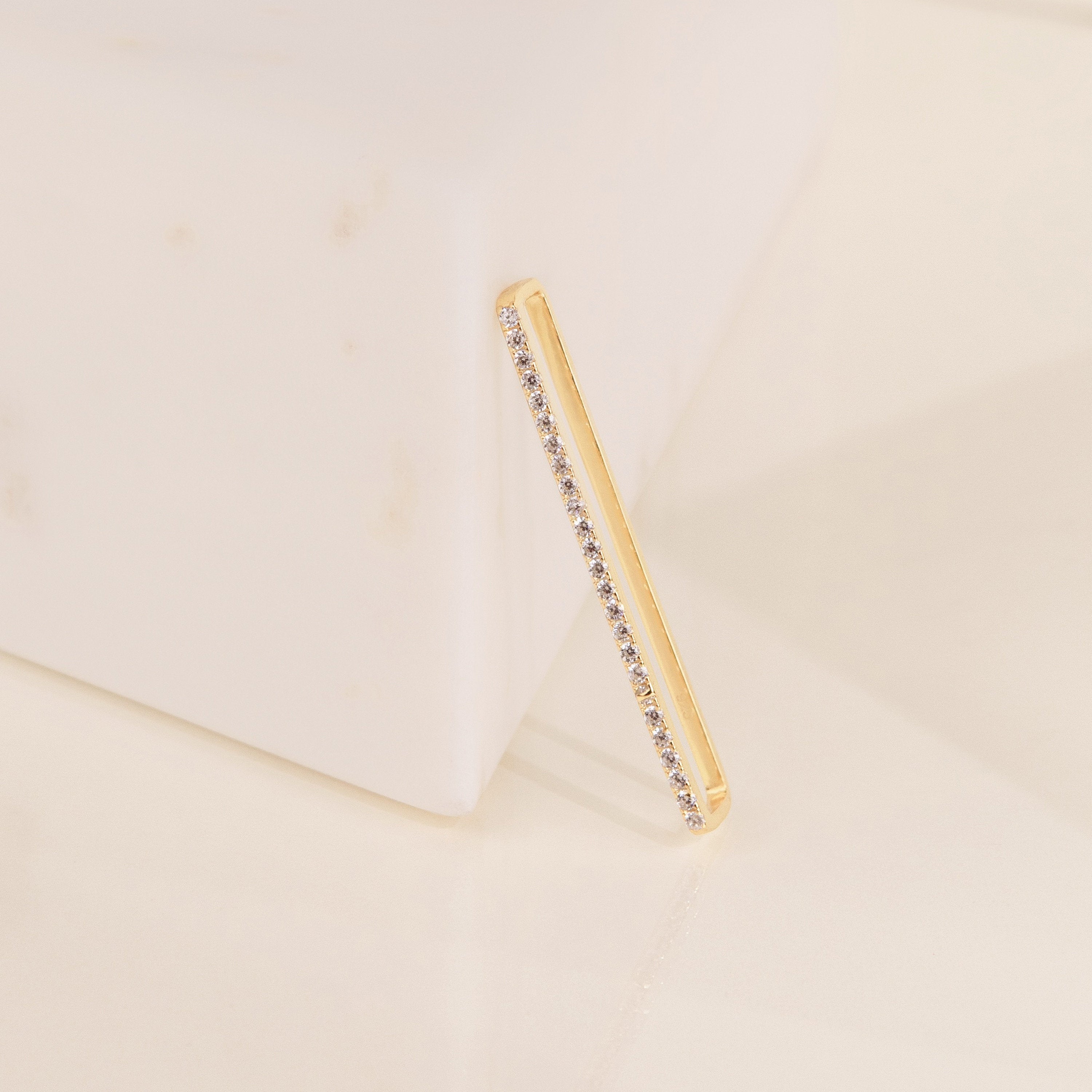 Bar Ear Cuffs with small gemstones rest against a white marble block on a cream background.